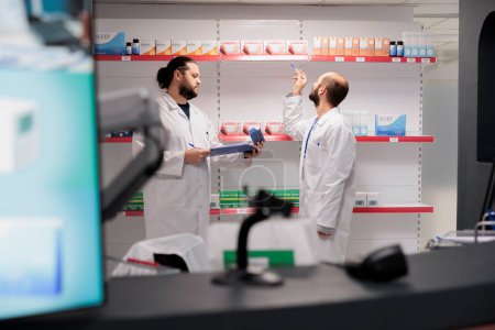 Photo for Two men pharmacists doing medicaments inventory checking pills packages, writing drugs information on papers. Pharmacy is a reliable and convenient location for filling prescription medication - Royalty Free Image