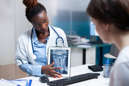 Photo for Specialist doctor delivering tomography medical exam results to patient in clinic office. Healthcare specialist showing radiography x-ray ct scan of cervical bone injury on tablet during check-up - Royalty Free Image