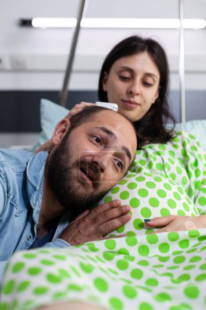 Foto de Cheerful future father standing with head on woman belly, talking with child before caesarean surgery in hospital ward. Pregnant patient preparing to delivery child in maternity facility - Imagen libre de derechos