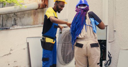 Téléchargez les photos : Knowledgeable professionals commissioned by client to work on broken air conditioner, dismantling condenser metal coil panel. Trained engineers opening hvac system to check for faulty components - en image libre de droit
