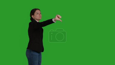 Téléchargez les photos : Side view of corporate employee giving thumbs down symbol in studio, doing dislike and negative bad gesture. Businesswoman with office suit expressing disapproval and disagreement on camera. - en image libre de droit