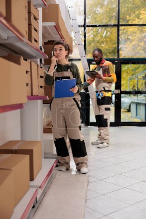 Photo for Storage room worker discussing products quality control with remote supervisor using landline phone in warehouse. Storehouse manager preparing customers orders, working at packages shipment - Royalty Free Image