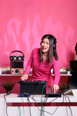 Photo for Musician mixing eletronic sounds with techno using professional turntables, having fun in studio over pink background. Artist performing song with electronics equipment and audio instrument - Royalty Free Image