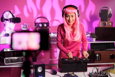 Photo for Cheerful artist standing at dj table in night club performing techno song using mixer console while filming music session with professional camera. Woman posting performance video on her channel - Royalty Free Image