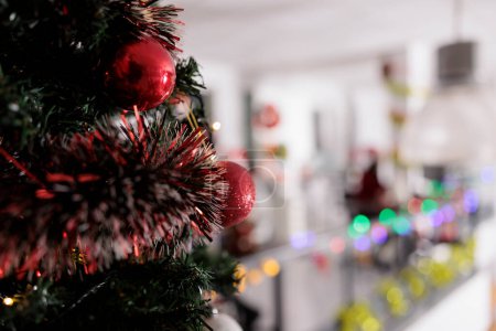 Foto de Enfoque de cerca en el árbol de Navidad decorado en rojo con la oficina moderna borrosa en el fondo. Lugar de trabajo profesional adornado listo para la temporada de vacaciones fiesta corporativa santa secreta - Imagen libre de derechos
