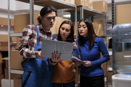 Photo for Postal warehouse asian employees team analyzing buyers order list on laptop. Storehouse man and women workers using parcel tracking system software and cooperating in storage room - Royalty Free Image