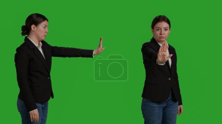 Photo for Close up of young manager showing stop talking sign with palm, expressing negative gesture and denial. Female worker in office suit doing rejection and refusal symbol over greenscreen backdrop. - Royalty Free Image
