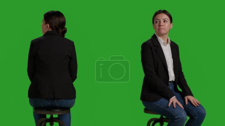 Téléchargez les photos : Gros plan du travailleur de l'entreprise qui attend sur la chaise avant d'assister à une réunion d'affaires, assis dans un studio avec fond vert. Femme habillée en costume de bureau travaillant comme employée ou gestionnaire. - en image libre de droit