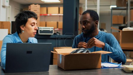 Foto de Small business partners packing merchandise in boxes and doing products quality control before shipping goods. Young woman signing logistics papers and man putting stock in packages. - Imagen libre de derechos