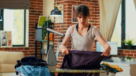 Téléchargez les photos : Unhappy person feeling exhausted of ironing laundered clothing, depressed housewife doing apartment chores. Young adult feeling tired about spring cleaning and doing housework alone. - en image libre de droit