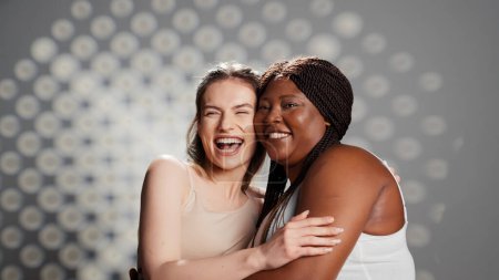 Téléchargez les photos : Filles lumineuses heureuses riant et posant en studio, créant une publicité pour la positivité et la diversité du corps. Modèles de soins de la peau avec différentes couleurs et types de corps favorisant la féminité et l'amour-propre. - en image libre de droit