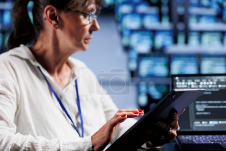 Photo for Aged system administrator writing script code in data center on laptop terminal. Skillful employee doing maintenance work in server room, updating racks software to prevent malfunctions - Royalty Free Image