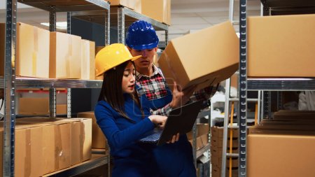 Photo for Asian employees checking stock goods on laptop, working with products on racks in storehouse depot. Team of people looking at inventory and merchandise logistics in storage room. - Royalty Free Image