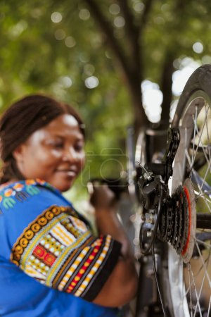 Photo for Selective focus on black woman repairing bicycle parts with professional tool in home yard. Detailed shot of bike rear derailleur and cogset being repaired and adjusted outside for leisure cycling. - Royalty Free Image