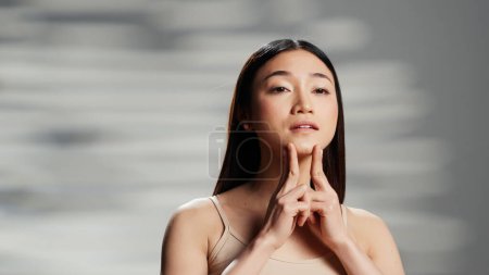 Photo for Confident model using moisturizing cream for routine, applying face serum on cheecks and promoting beauty cosmetics or products. Gentle woman with luminous radiant skin, self love. - Royalty Free Image
