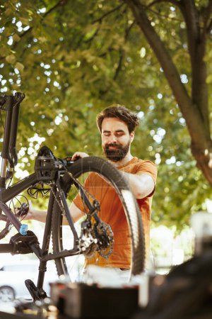 Photo for Enthusiastic male cyclist upkeeping and servicing bicycle in home yard. Dedicated sporty caucasian man inspecting and performing bike maintenance for outdoor leisure cycling. - Royalty Free Image