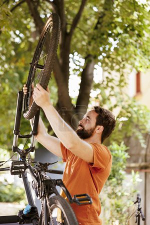 Photo for Active sports-loving man ensures bike wheel is secure for summer outdoor leisure cycling. Healthy committed caucasian male cyclist safely reattaching bicycle tire in home yard. - Royalty Free Image