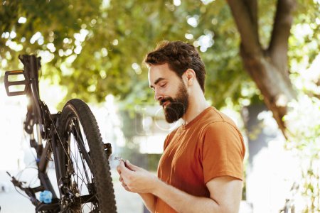 Téléchargez les photos : Homme caucasien sportif entretenant son vélo à l'extérieur comme entretien estival annuel. Cycliste masculin sportif travaillant avec un outil professionnel pour entretenir et réparer le vélo moderne en plein air. - en image libre de droit
