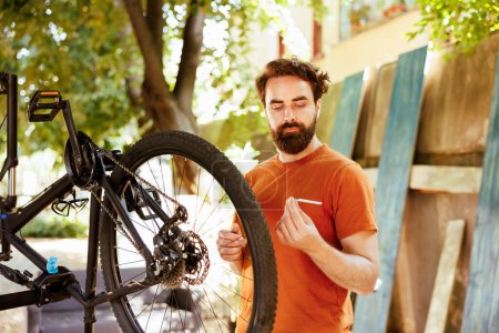Téléchargez les photos : Homme énergique en bonne santé réparer son propre vélo dans la cour, faire l'entretien extérieur annuel du véhicule avec des outils professionnels. Examen de l'équipement de vélo à fixer, activité de loisirs pendant l'été. - en image libre de droit