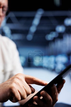 Photo for Old IT developer using tablet in high tech facility, installing dedicated VPN servers able to provide encrypted sensitive data, online anonymity and fast speed bandwidth to clients, close up - Royalty Free Image