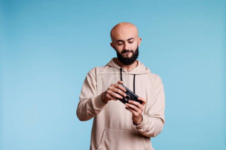 Photo for Concentrated arab man playing online game on smartphone. Young carefree bald bearded gamer enjoying leisure time and having fun while using videogame application on mobile phone - Royalty Free Image