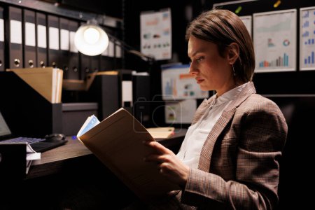 Photo for Caucasian inspector reading criminology report, working overtime at criminal case in arhive room. Private detective analyzing crime scene evidence, searching for new clues to catch suspect - Royalty Free Image