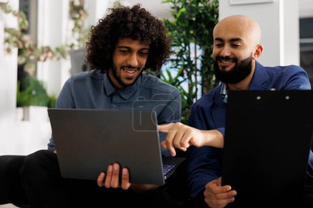 Téléchargez les photos : Des hommes d'affaires arabes collaborent à un projet de démarrage et vérifient les données financières sur un ordinateur portable dans un espace de coworking d'entreprise. Deux collaborateurs planifiant les objectifs de l'entreprise dans le bureau d'affaires - en image libre de droit