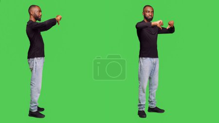 Téléchargez les photos : Homme mécontent montrant les pouces vers le bas geste à la caméra, faisant désaccord et signe de désapprobation en studio. Décontracté adulte posant sur fond plein corps écran vert, n'aime pas symbole négatif. - en image libre de droit