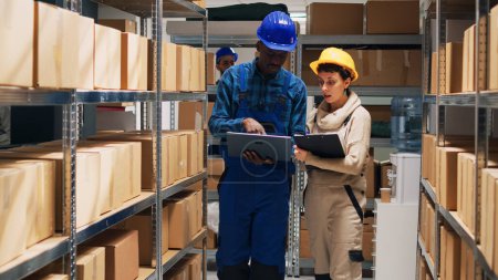 Photo for Multiethnic team of employees working with goods and checking stock inventory on laptop, cargo in storage room. Depot workers analyzing industrial goods to plan distribution and shipment. - Royalty Free Image