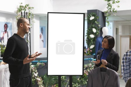 Photo for Clothing store worker and client discussing clothing brand collection while standing near ads whiteboard mockup. Boutique consultant using digital display to show apparel options to customer - Royalty Free Image