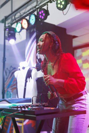 Woman dj interacting with audience and speaking from stage while performing in nightclub. African american musician singing and playing electronic music at discotheque party in club