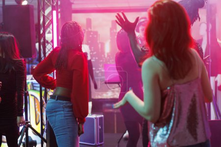 People partying at disco gathering and enjoying nightlife activity in nightclub. Diverse men and women dancing and celebrating while moving to modern music rhythm in club