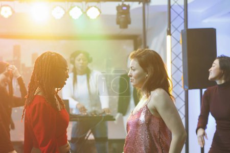 Téléchargez les photos : Les jeunes femmes qui font une bataille de danse lors d'une fête disco avec de la musique électronique en direct dans une boîte de nuit. Des danseurs sérieux debout sur la piste de danse bondée et improvisant des mouvements à la discothèque - en image libre de droit