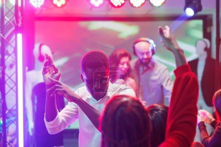 Téléchargez les photos : Homme dansant avec des amis et faisant la fête dans une discothèque. Jeune clubber afro-américain s'amuser et faire des mouvements sur la piste de danse lors d'un concert de musique électronique en club - en image libre de droit