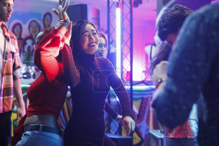 Cheerful smiling diverse women dancing together and laughing while partying and enjoying nightlife in club. Happy girlfriends having fun and celebrating on dancefloor in nightclub