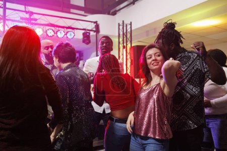 Foto de Pareja multiracial bailando juntos mientras festejan en un club nocturno lleno de gente. Hombre y mujer club y divertirse en la pista de baile iluminado con focos en discoteca club - Imagen libre de derechos