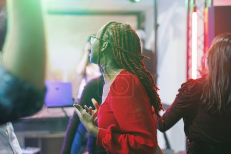 Woman dancing with friends while partying on dancefloor with spotlights in nightclub. Young african american girl in red blouse having fun and enjoying discotheque in club