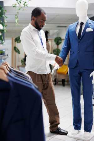 Photo for Assistant adjusting jacket on mannequin wearing formal outfit in clothing store. African american man checking male suit on model showcasing apparel for customers in shopping mall - Royalty Free Image