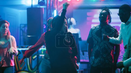Photo for Young woman dancing at nightclub, feeling cheerful on music at the bar. Group of friends showing funky dance moves in the club, partying together on dance floor with lights. Tripod shot. - Royalty Free Image