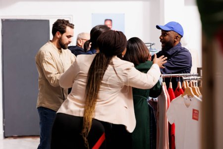 Foto de Agente de seguridad afroamericano estresado parado en la entrada de la tienda de ropa manejando la multitud de compradores que irrumpen en la tienda el Viernes Negro. Loco Los clientes enojados esperando en la cola para las ventas - Imagen libre de derechos