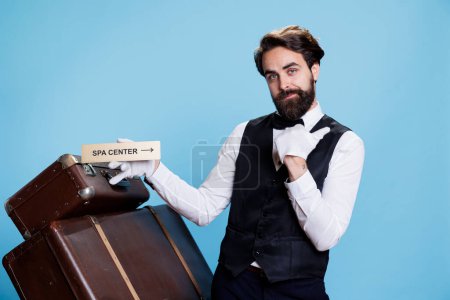 Photo for Hotel employee works in travel sector and leads visitors to the relaxation area using indication for the spa. Stylish man in formal attire indicating and displaying pointer with locations. - Royalty Free Image