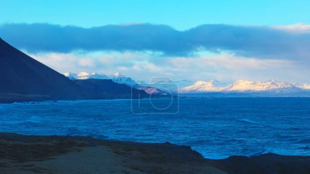 Photo for Majestic landscape of black sand beach in iceland, panoramic view of snowy mountains and freezing cold waters. Beautiful icelandic scenery on coastline shore with ocean waves. Handheld shot. - Royalty Free Image