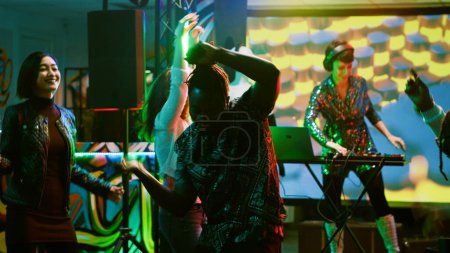 Foto de Hombre afroamericano bailando en el club, disfrutando de una reunión social con amigos en la pista de baile. Grupo de personas que se divierten sintiéndose alegres en la discoteca, escuchando música disco. Trípode tiro. - Imagen libre de derechos