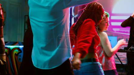 Téléchargez les photos : Groupe multiethnique de personnes dansant dans une discothèque, s'amusant avec de la musique électronique sur la piste de danse. Foule d'amis sautant et faisant la fête à la boîte de nuit, projecteurs disco. - en image libre de droit