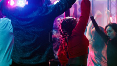 Photo for Cheerful persons jumping at nightclub, having fun partying on electronic mixing music at modern party. Cool people enjoying night out on club dance floor, live show performance. Tripod shot. - Royalty Free Image