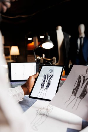 Photo for Couturer looking for inspiration for upcoming bespoke comissioned exquisite dress, comparing handdrawn sketch with online outfit. Tailor analyzing designs of fashion attire in tailoring studio - Royalty Free Image