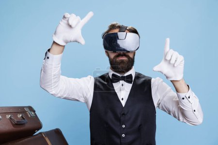 Photo for Modern doorkeeper using vr headset against blue background, enjoying 3d interactive vision experience. Professional bellboy hotel worker having fun with virtual reality glasses. - Royalty Free Image