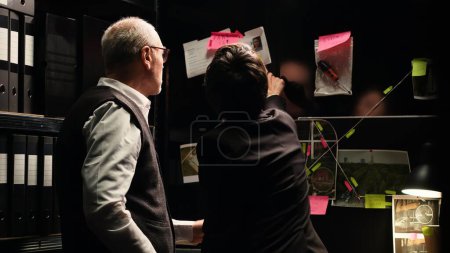 Photo for Police agents examine evidence board in investigation office, analyzing unearthed clues to build case file. Detectives team working with classified documents and records to catch suspect. - Royalty Free Image