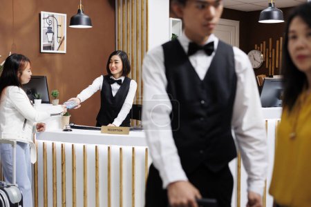 Tourist arrives on holiday destination and pays for resort room at the reception desk. smiling asian receptionist hands over POS for accommodation payment at welcoming hotel