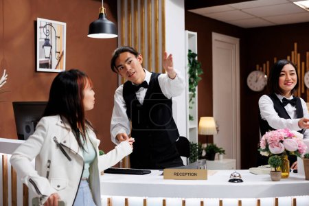 Photo for Woman being guided by helpful asian receptionist while on holiday in modern hotel lobby. Traveler starting trip in entrance of extravagant resort, receiving room card key - Royalty Free Image